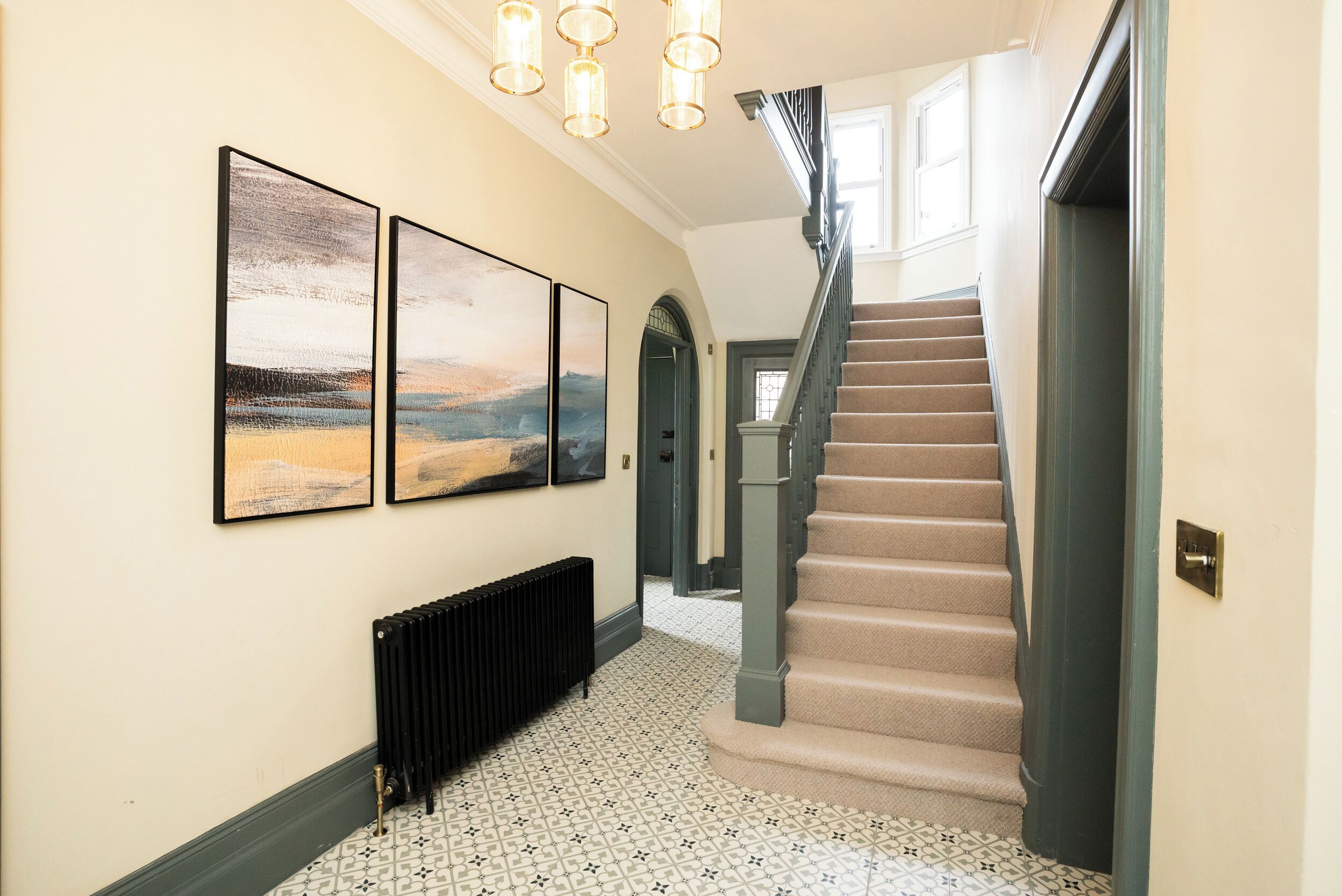 A hallway with a staircase, tiled floor, and three framed artworks on the wall.