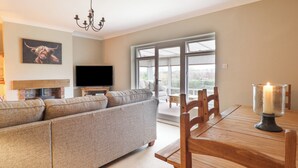 A modern living room with a sectional sofa, a flat-screen TV, a fireplace, and a dining table with chairs. - The Crib (Llandudno)