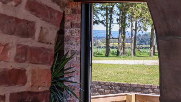 A brick wall with a window overlooking a grassy area with trees and a distant view of hills. - Molly's Cottage (Malton)