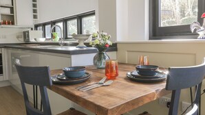 A modern kitchen with a wooden dining table, two chairs, and a vase of flowers. - Cherry Orchard Farm (Maidstone)