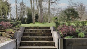 A set of concrete steps leading up to a wooden fence, surrounded by a garden with various plants and trees. - Cherry Orchard Farm (Maidstone)