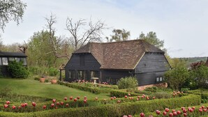 A black wooden house with a sloped roof surrounded by a well-maintained garden with red tulips. - Cherry Orchard Farm (Maidstone)