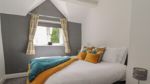 A bedroom with a bed, a window with curtains, a bedside table with a lamp, and a grey carpet. - Stork Cottage (Lancaster)