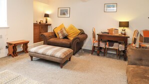 A cozy living room with a brown leather sofa, a wooden coffee table, and a patterned ottoman. There is a small wooden side table and a lamp on a side table. - Stork Cottage (Lancaster)