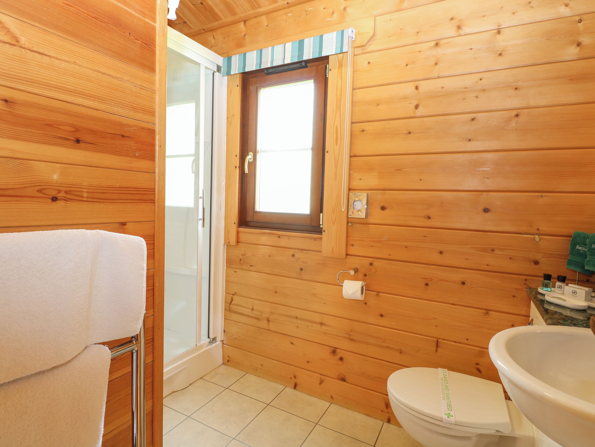Une salle de bain rustique, aménagée dans une cabane en bois, avec des toilettes, une douche et une fenêtre.