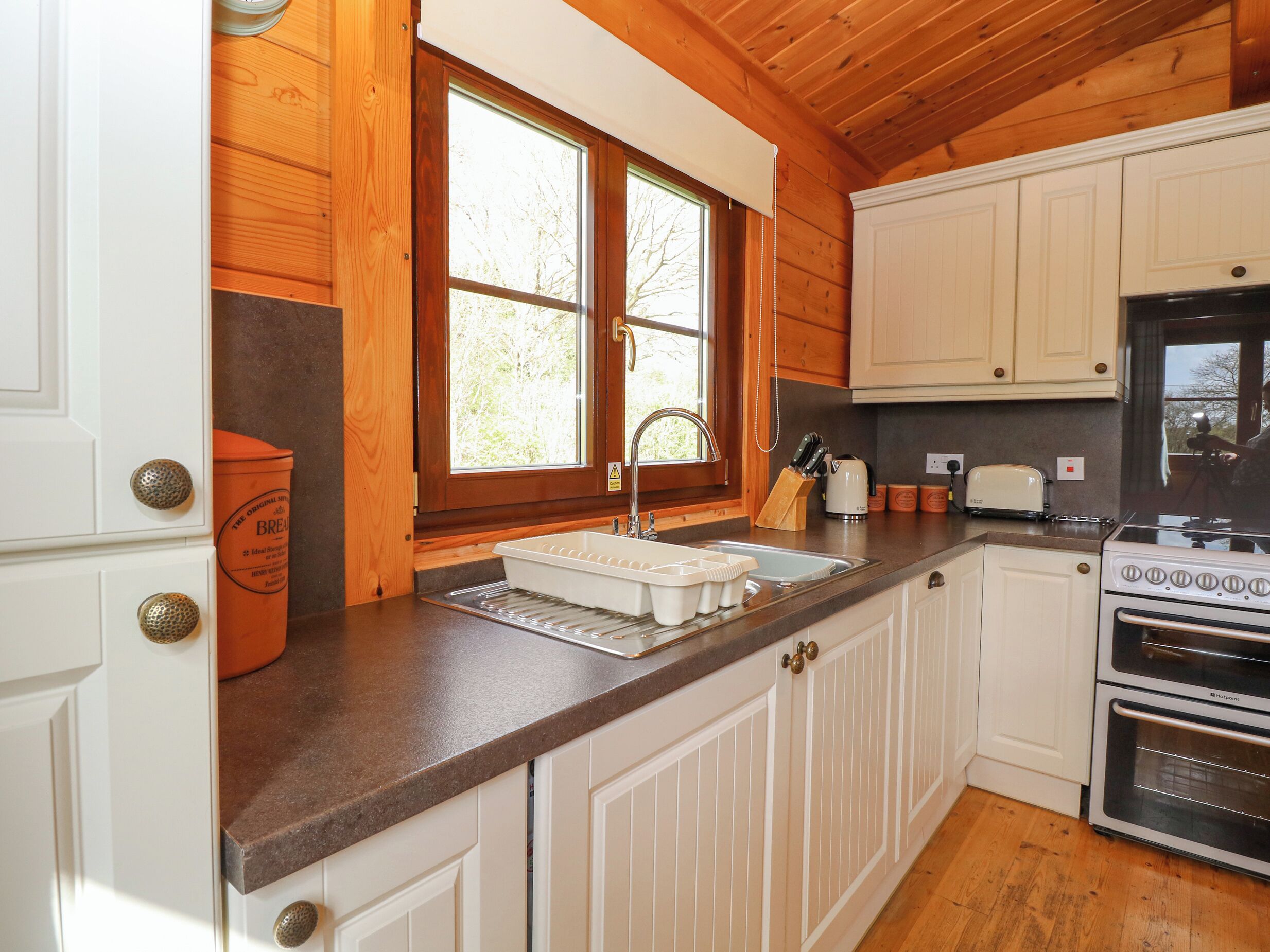 Una cocina con gabinetes de madera, un lavamanos, una estufa y una ventana con persianas.