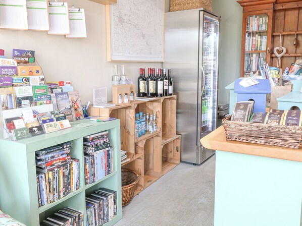 A bookstore with shelves of books, a refrigerator with wine bottles, and a wooden counter with magazines. - Wagtail Lodge (Bury St Edmunds)