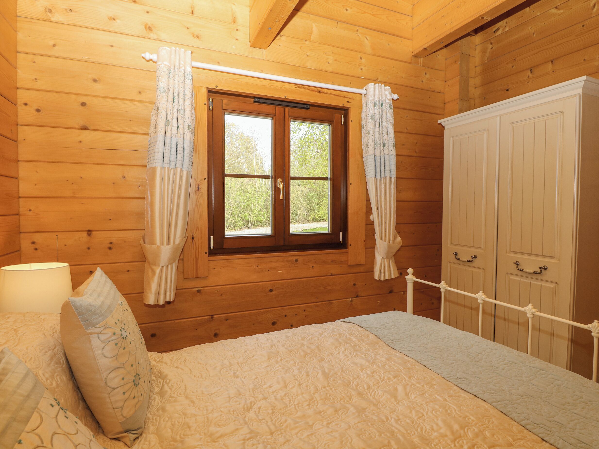 A wooden room with a bed, a window with curtains, and a wardrobe.