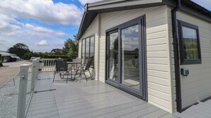 A modern building with large sliding glass doors, a deck with outdoor furniture, and a clear sky. - Lodge 3 (Saint Asaph)