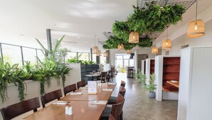 A modern restaurant with long wooden tables, dark cushioned seating, and hanging plants. - Lodge 3 (Saint Asaph)
