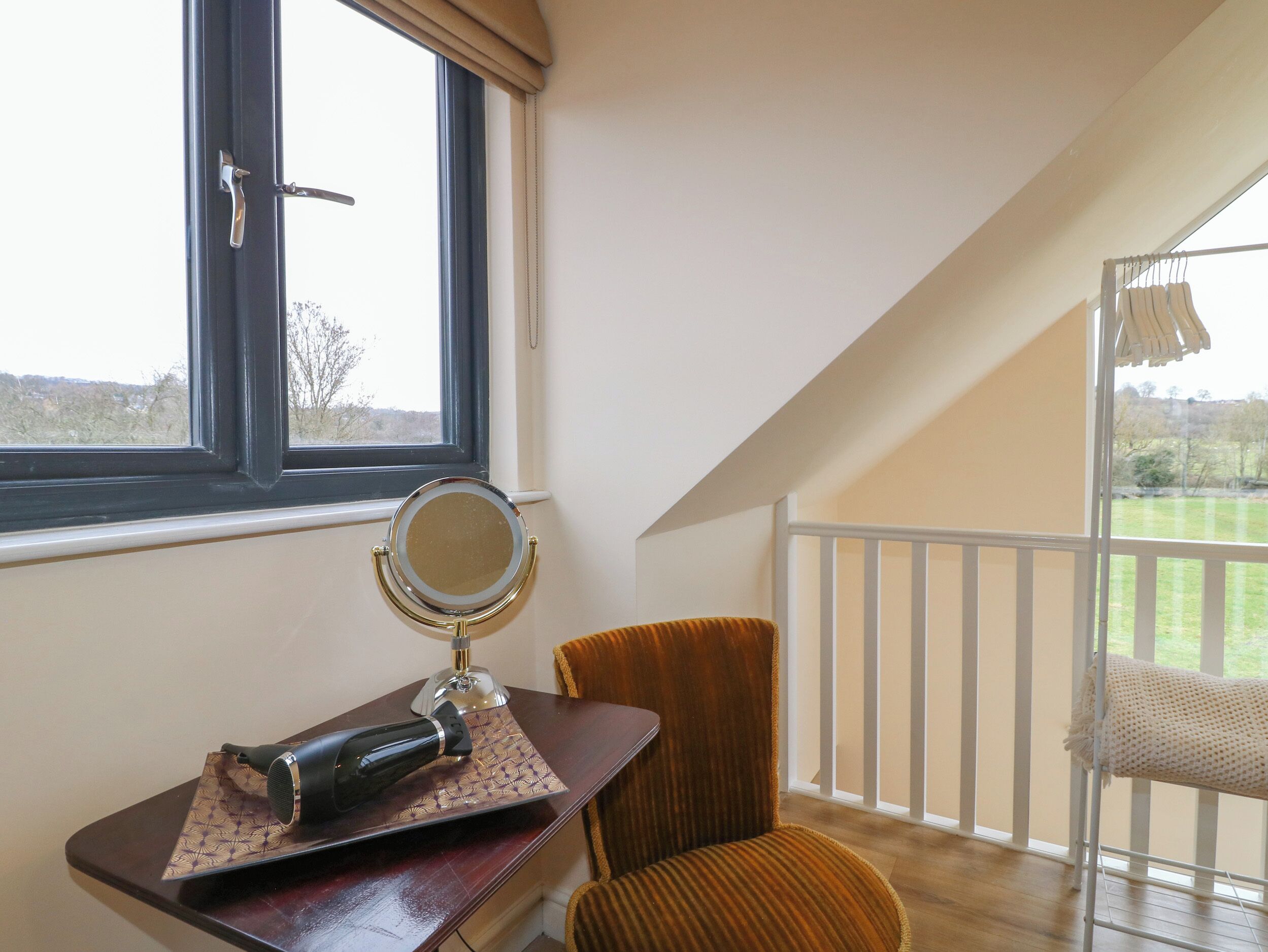 A room with a wooden desk, a chair, a window with a view of the outdoors, and a balcony with a railing.