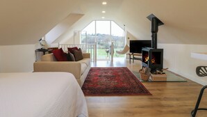 Une chambre spacieuse, aménagée en style « loft », avec un grand lit, un canapé, une télévision, une cheminée et une vue sur l’extérieur.