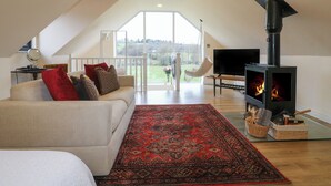 Une chambre spacieuse de style loft, dotée d’une grande fenêtre, d’un canapé confortable, d’un téléviseur à écran plat et d’un poêle à bois.