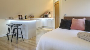 Une chambre compacte comprenant un lit, une petite kitchenette et un coin repas avec des tabourets.