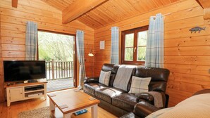 A wooden cabin interior with a leather sofa, a TV, and a wooden table. - Kingfisher Lodge (Bury St Edmunds)
