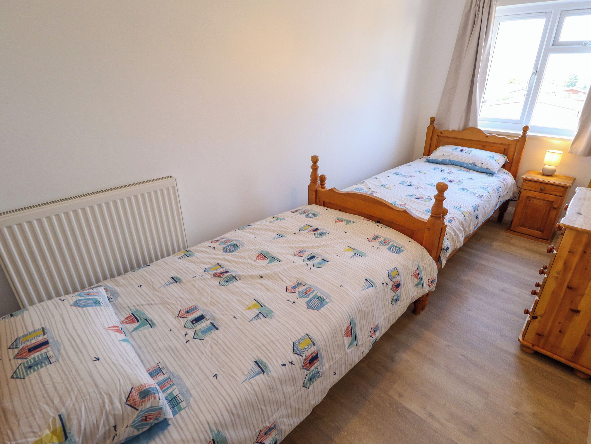 Ein Schlafzimmer mit einem Einzelbett, einem Nachttisch mit Lampe, einem Heizkörper und einem Fenster mit Vorhängen.