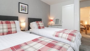 A hotel room with two beds, a nightstand with a lamp, a framed picture on the wall, and a door leading to another room. - The Penthouse (Windermere)