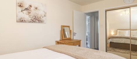 Une chambre à coucher avec un lit, un miroir, une table de chevet en bois et un tableau accroché au mur.