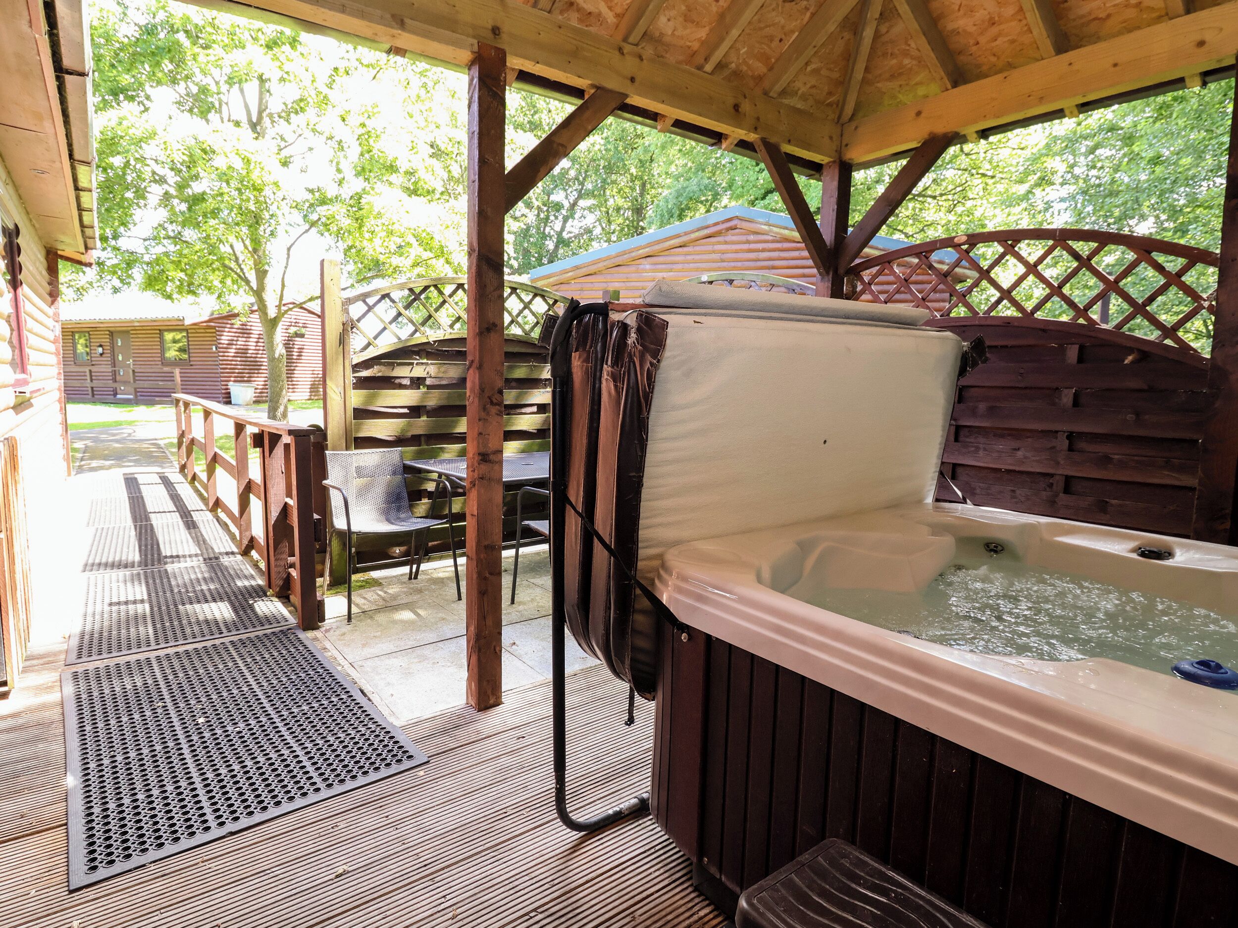 A hot tub under a wooden pergola with a wooden fence and a table with chairs.
