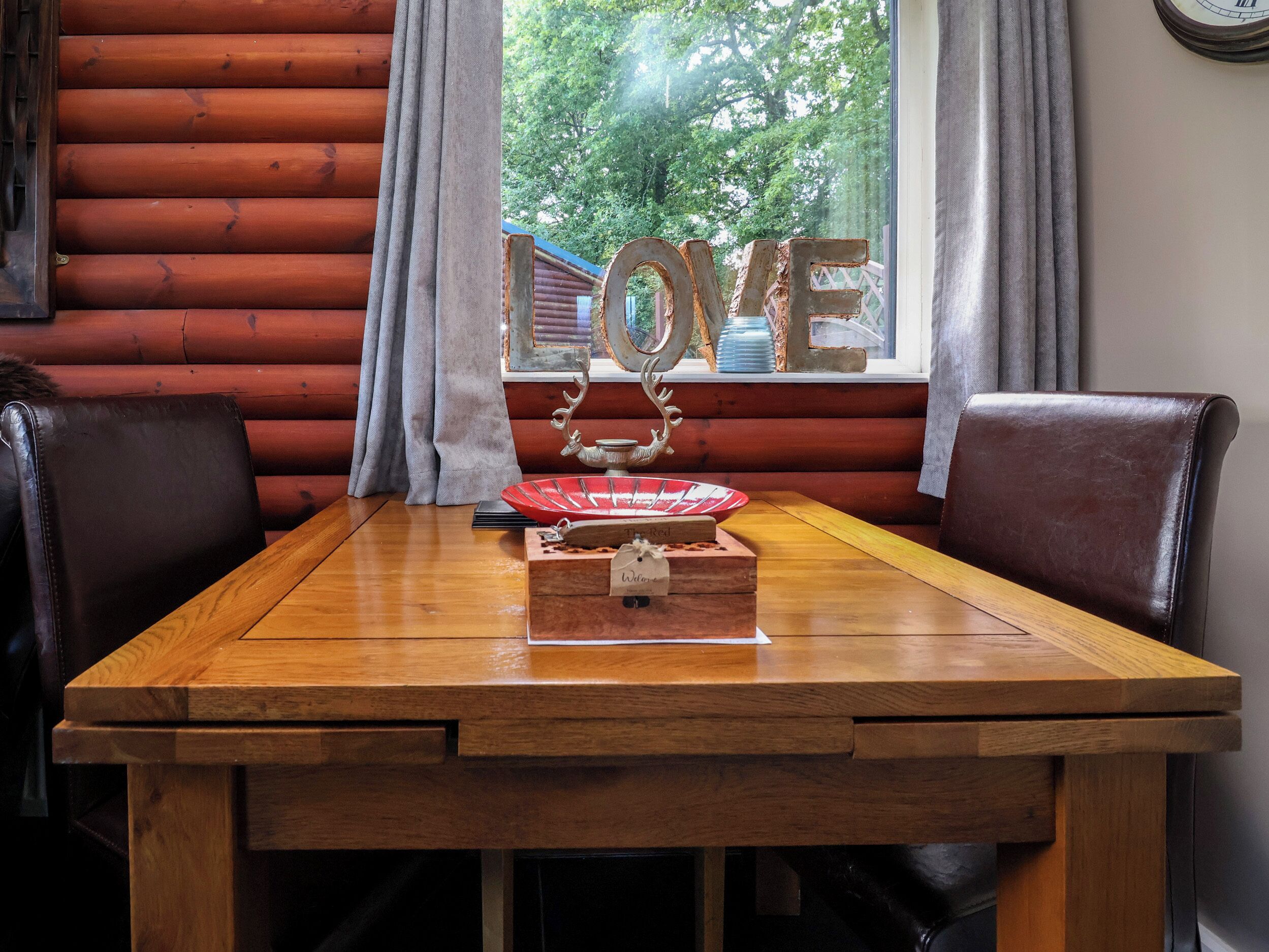 A wooden table with a decorative centerpiece, a window with curtains, and a view of greenery outside.