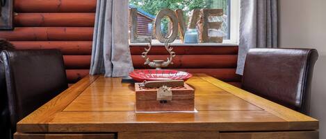 A wooden table with a decorative centerpiece, a window with curtains, and a view of greenery outside.