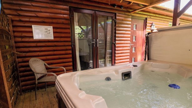 Uma cabana de toras com hidromassagem, uma cadeira de vime e um deck de madeira.