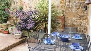 A patio with a table set for dining, surrounded by various plants and a stone wall.