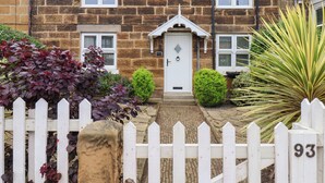 A stone house with a white picket fence, a front door, and a number '93' on the fence.