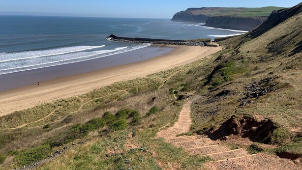 A coastal landscape with a sandy beach, a rocky cliff, and a sea wall.