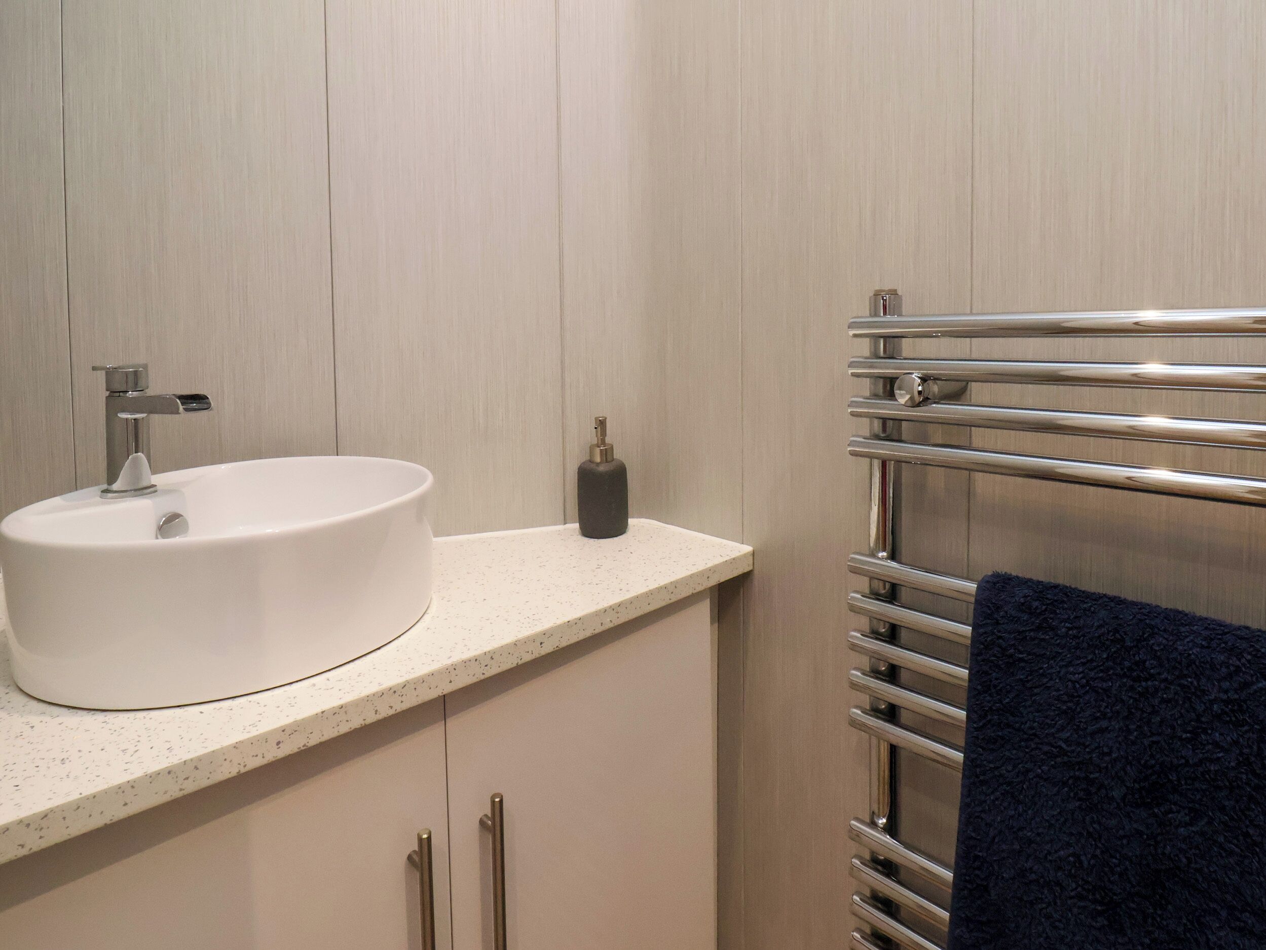 A bathroom with a white sink, a faucet, a soap dispenser, and a towel rack with a dark towel.