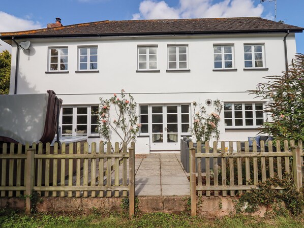 A two-story white house with a front door, multiple windows, and a wooden fence. - Culver Court Cottage (Crediton)