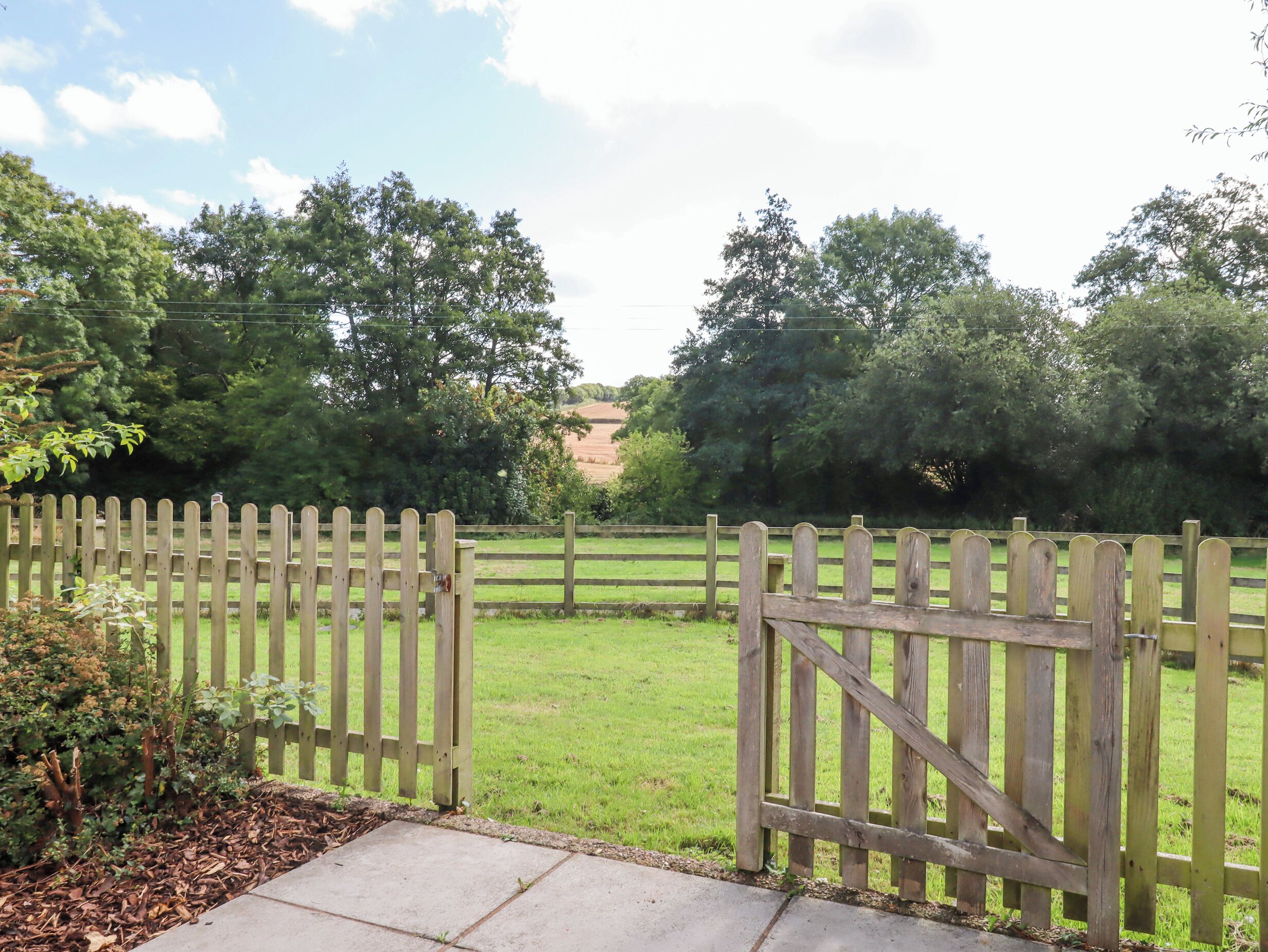 A wooden gate leading to a grassy area with trees and a hill in the background.