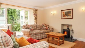 A cozy living room with a plaid sofa, a wooden coffee table, and a fireplace. - Culver Court Cottage (Crediton)