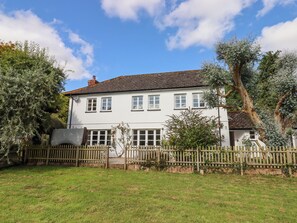 A white two-story house with a tiled roof, surrounded by a wooden fence and trees. - Culver Court Cottage (Crediton)