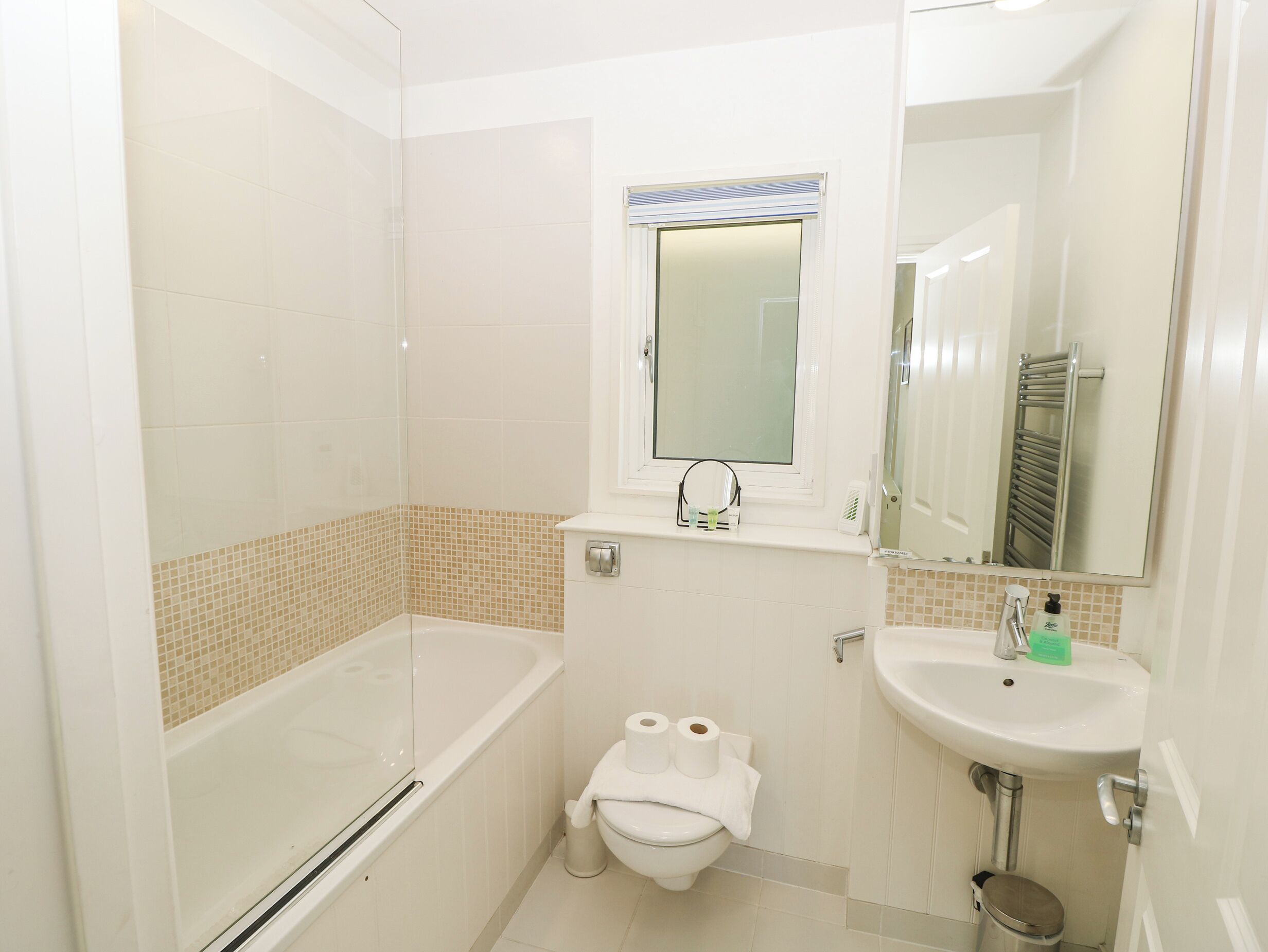 A small bathroom with a bathtub, toilet, sink, and a window with a towel rack.