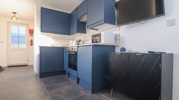 A modern kitchen with blue cabinets, a black refrigerator, a microwave, and a flat-screen TV mounted on the wall.