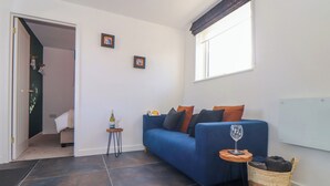 A modern living room with a blue sofa, a small side table with a glass, and a wicker basket. - Fifty Degrees North (Penzance)