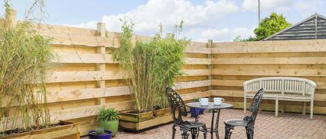 A patio with a wooden fence, a white bench, and metal chairs around a small table.