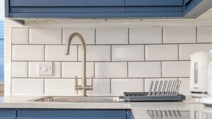 A kitchen with a stainless steel faucet, white tiled backsplash, and blue cabinets. - Fifty Degrees North (Penzance)
