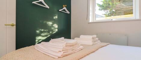A neatly made bed with folded towels and two white hangers on a dark green wall.