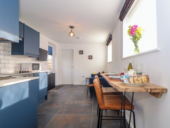 Une cuisine moderne avec des armoires bleues, un four à micro-ondes encastré et un coin repas comprenant une table et des chaises en bois.