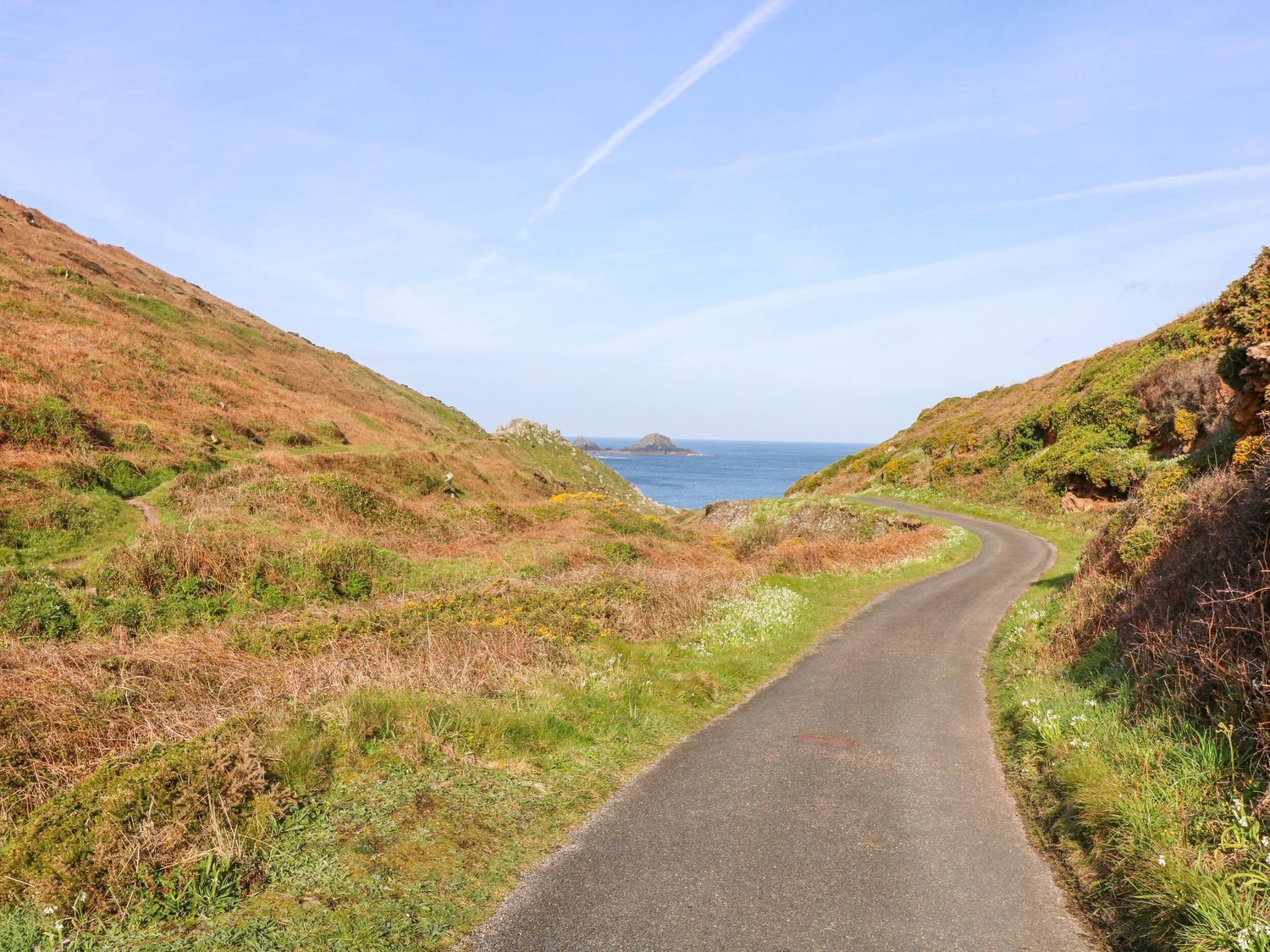 A narrow, winding road flanked by grassy hills and a clear blue sky.