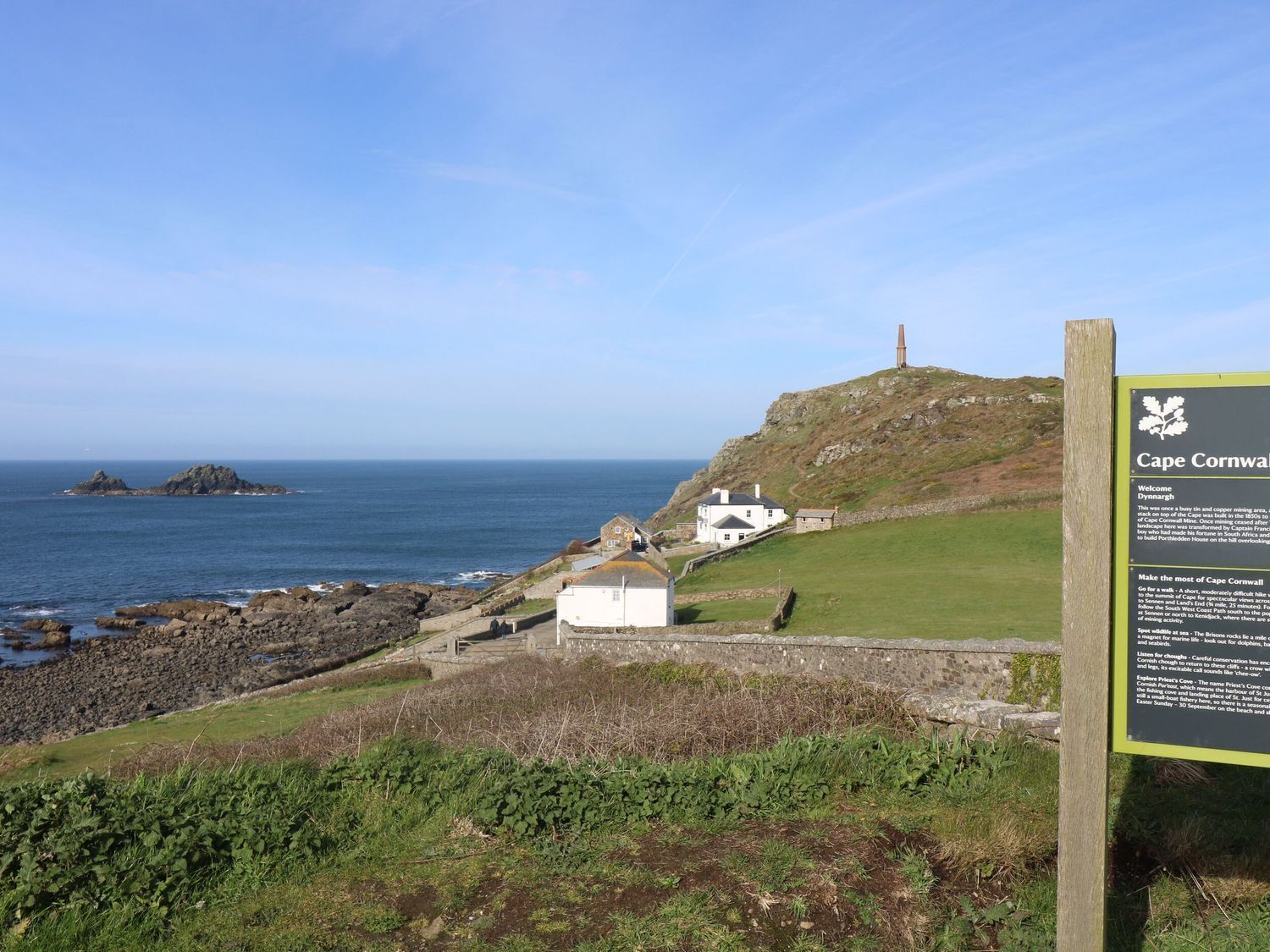 A coastal view with a signboard, rocky shoreline, and a lighthouse.