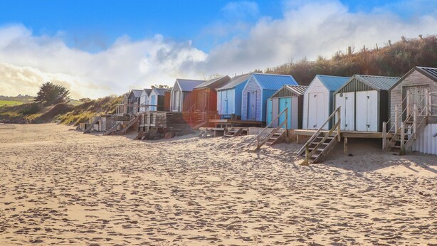 A row of beach huts with wooden stairs leading up to them, situated on a sandy beach with a clear sky. - Mor Glas (Pwllheli)