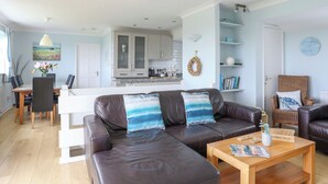 A modern living room with a leather sofa, wooden coffee table, and a dining area with a white table and chairs. - Mor Glas (Pwllheli)