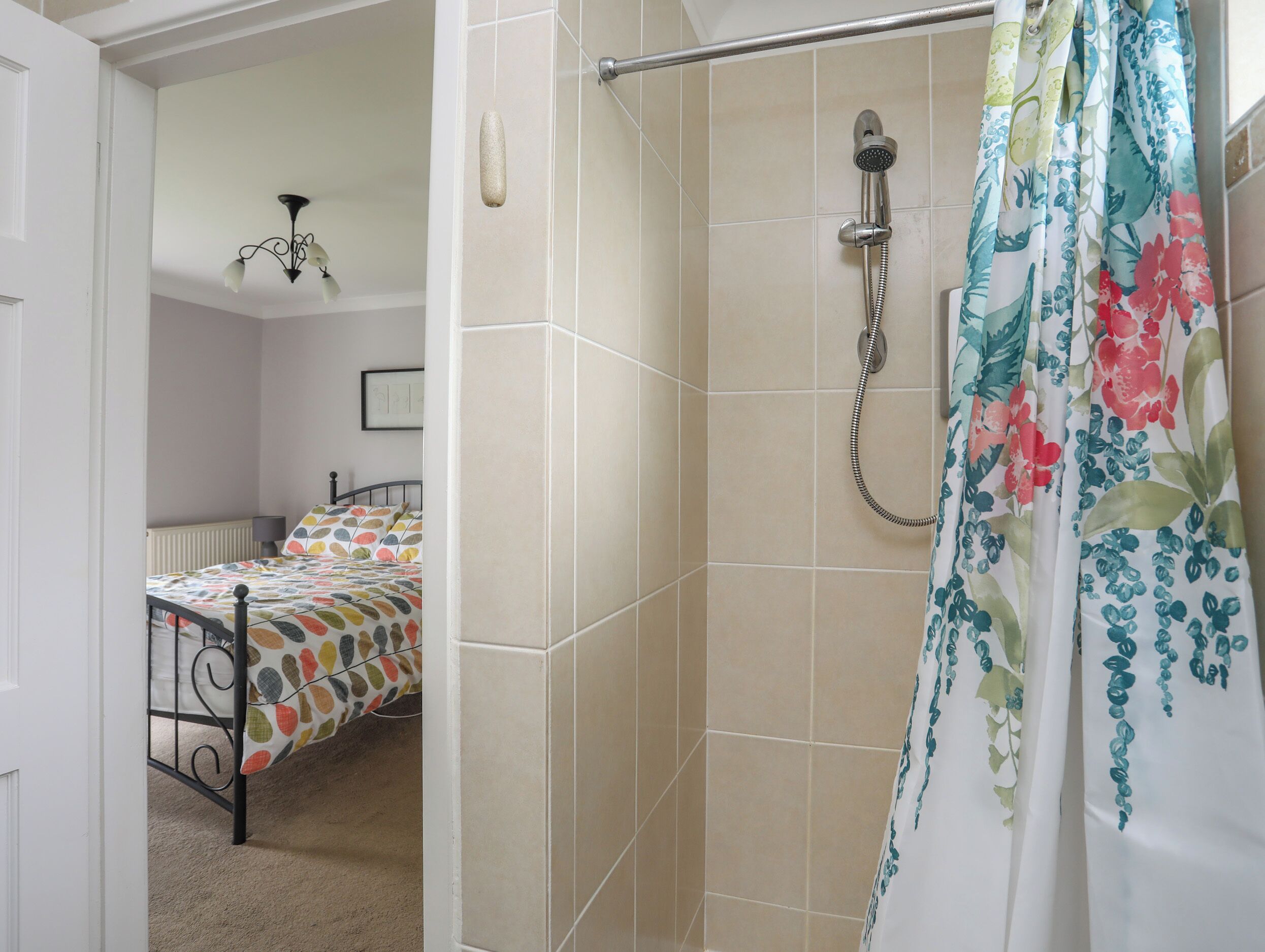 Un baño con ducha, paredes con azulejos, una cama con colcha de colores y una puerta que da a otra habitación.