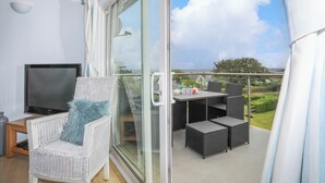 A balcony with a TV, wicker furniture, and a view of the sea. - Mor Glas (Pwllheli)