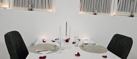 A dining table set for two with candles, glasses, and a centerpiece.