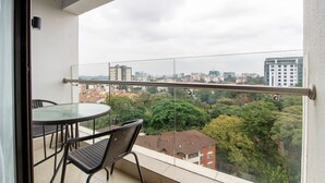En balkon med gelænder af glas, et rundt bord og to stole.