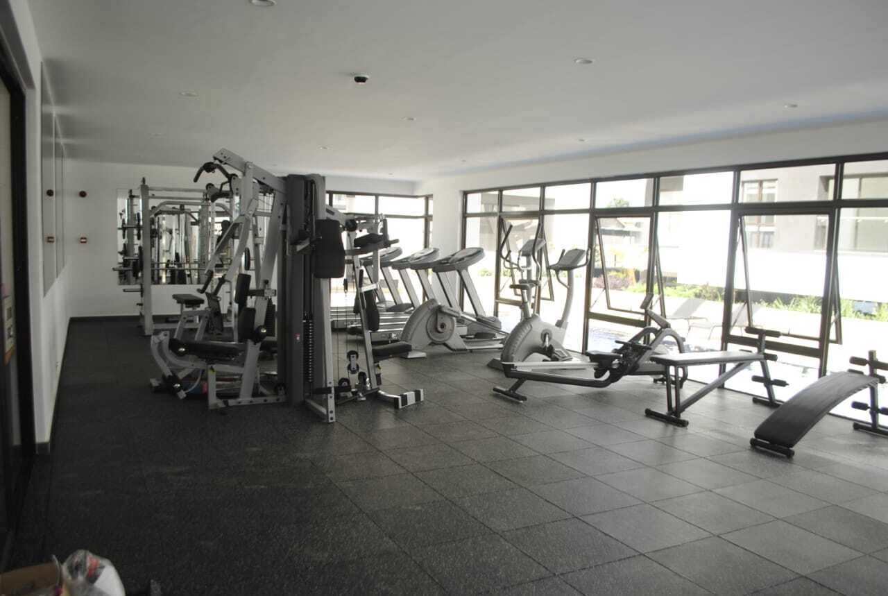 Ein Fitnessstudio mit verschiedenen Trainingsgeräten, großen Fenstern und einem gefliesten Boden.